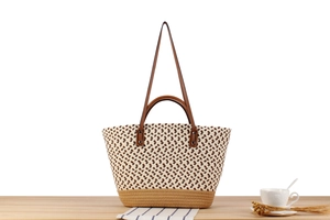 Detailed view of woven straw tote bag with brown leather handles on wooden table