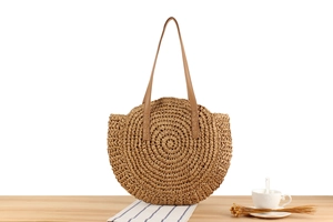 Detail showing the spiral woven texture of the straw tote bag with brown leather shoulder strap