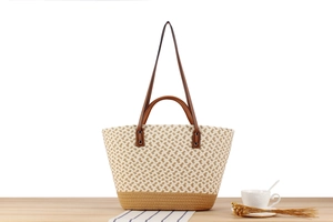 Close-up of bohemian woven straw tote bag with brown leather straps on wood surface