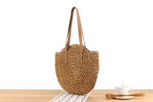 Detailed view of the woven paper rope texture and brown leather strap on round straw bag