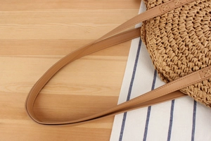Close-up of natural woven paper straw bag showing brown leather strap and fine texture