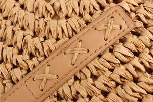 Detail of round woven paper straw bag with brown leather strap and intricate stitching