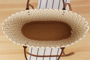 Top view of woven straw tote bag with brown leather handles on a wooden table