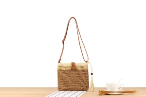 Detail of woven straw crossbody bag with leather strap, tassel and wooden beads