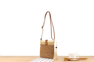 Detail of woven straw crossbody bag featuring leather strap and bohemian tassel accents