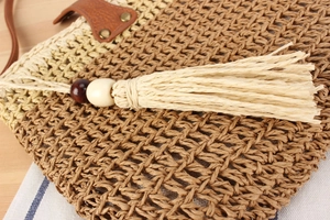 Detailed macro view of woven straw tote bag with beaded tassels and leather handle