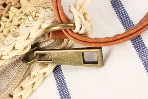 Detail of woven straw bag with premium brown leather strap and bronze metal zipper closure