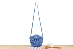 Détail d'un mini sac seau tressé bleu avec motifs ajourés sur une table en bois