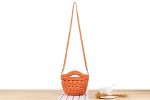 Détail du sac seau orange tressé à la main avec motif ajouré posé sur une table en bois