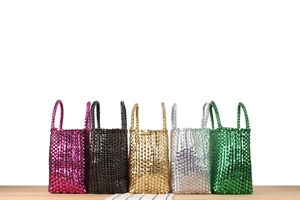 Vue détaillée de sacs à main tissés métalliques en cinq couleurs sur une table en bois