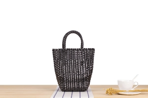 Détail d'un sac à main tissé noir en plastique avec poignée posé sur une table en bois