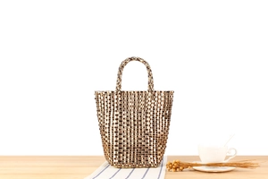 Détail d'un sac cabas tissé doré sur une table en bois avec une tasse de café blanc