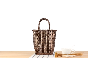 Détail d'un sac cabas tressé en plastique bronze posé sur une table en bois