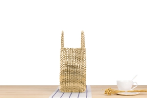 Vue détaillée d'un sac à main tissé doré avec texture en damier sur une table en bois