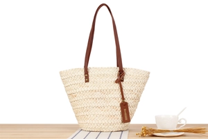 Detail of the woven straw tote bag texture and brown leather strap on a wooden table