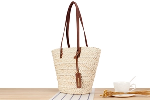 Detail of woven straw tote bag with brown leather handles on a minimal wooden table