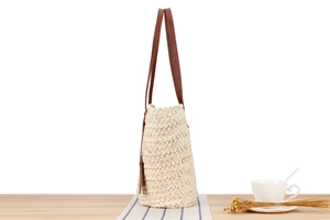 Detailed side view of beige woven straw tote bag with brown leather handles on a table