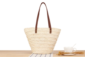 Detail of hand-woven straw tote bag with brown leather handles and rustic metal rivets