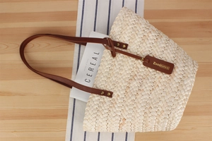 Detailed view of woven straw tote bag with brown leather handles and golden rivet accents