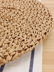 Handwoven moon-shaped bohemian straw handbag on a natural wood and striped cloth background