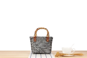 Detail of woven handbag featuring natural bamboo U-handle and leather rivet accents