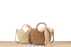 Detail of woven half-moon straw bags in beige and brown with lace bow on wooden desk