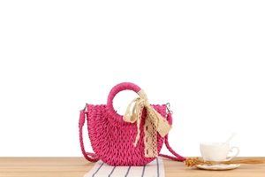 Detail of rose pink woven straw handbag with lace ribbon on rustic wooden table