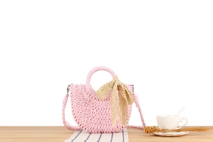 Close-up of pink woven half-moon handbag with lace bow on a wooden table setup