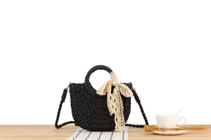 Detail of black woven crescent bag featuring a cream lace bow and matching strap