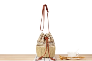 Detail of woven straw bucket bag with knit waves and long tassel drawstring on wood table