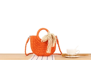 Detail of orange woven semi-circle straw bag with beige lace bow and long strap