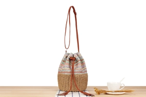 Detail of colorful woven straw bucket bag with brown leather strap and tassel closure