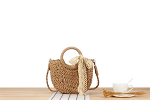 Detail of a woven straw semi-circle handbag with a beige lace scarf on a wooden table