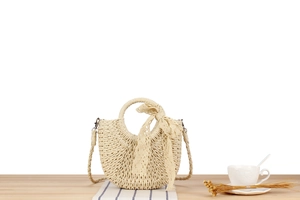 Detail of a beige woven half-moon bag with lace bow and round handle on a wooden table