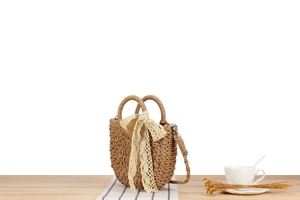 Detailed view of handmade woven straw bag with beige lace bow on a rustic wooden table