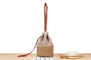 Detail of multi-colored woven bucket bag with leather strap and tassel on wooden surface