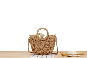 Detail of half-moon woven straw bag with lace bow and woven strap on a wooden surface