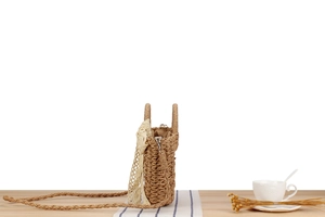 Detail of woven straw bag featuring delicate lace ribbon and rustic wooden table decor
