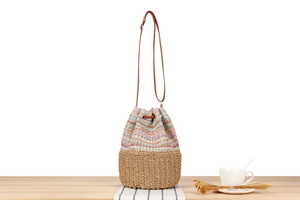 Detail of multi-color woven straw bucket bag with drawstring closure and leather strap