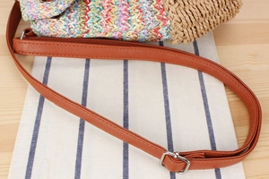 Detail of colorful woven straw bag featuring brown faux leather strap and metal buckle