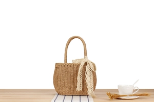 Detailed straw woven bag featuring cream lace ribbons on a soft blue striped cloth