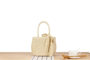 Detail of hand-woven paper rope bag featuring a cream lace bow on a rustic wooden table
