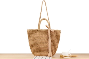 Close-up of bohemian woven paper rope beach bag with pink ribbon bow on a wooden surface
