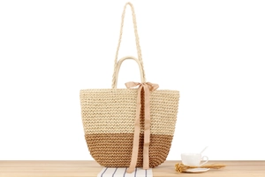 Detail of bohemian paper straw tote bag featuring contrast stitching and ribbon bow