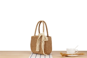 Detail of straw woven handbag featuring cream lace bow and natural fiber texture