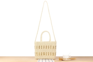 Close-up of cream woven beach tote featuring gold stripe details and versatile straps