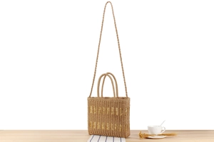 Detail of hand-woven straw beach tote with gold thread stripes on a wooden table
