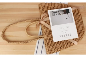 Close-up of bohemian woven straw bag with soft silk bow on light wood tabletop
