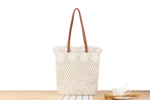 Detail view of cream crochet tote bag with hollow pattern and brown leather handles