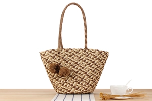 Detail of geometric pattern straw bag with brown pom poms and rope handles for vacation
